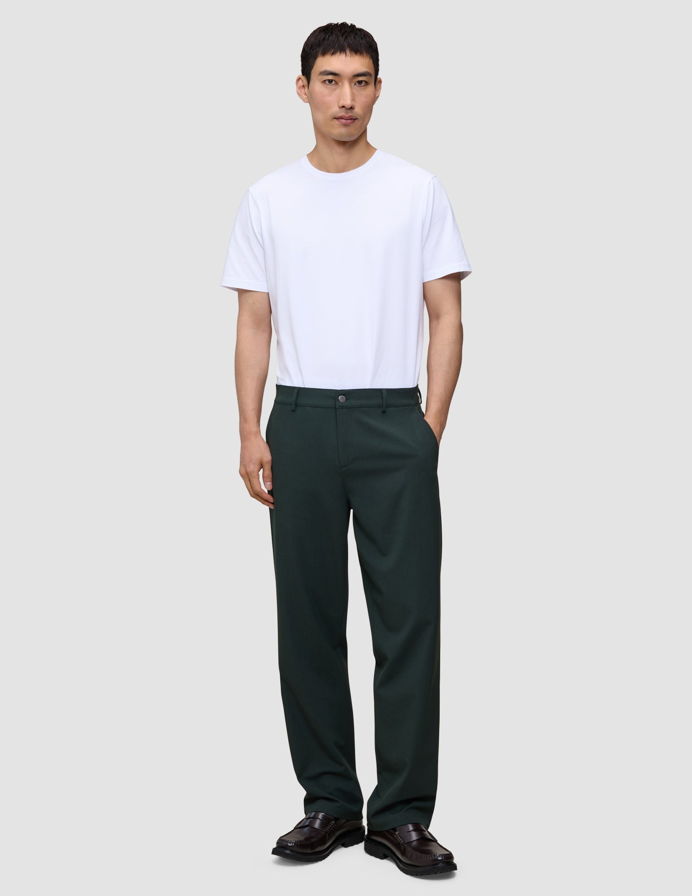 Eine Person, die ein weißes T-Shirt, dunkle Slipper und die Ease Pants Relaxed Fit Northern Pine mit 360°-Stretch trägt.